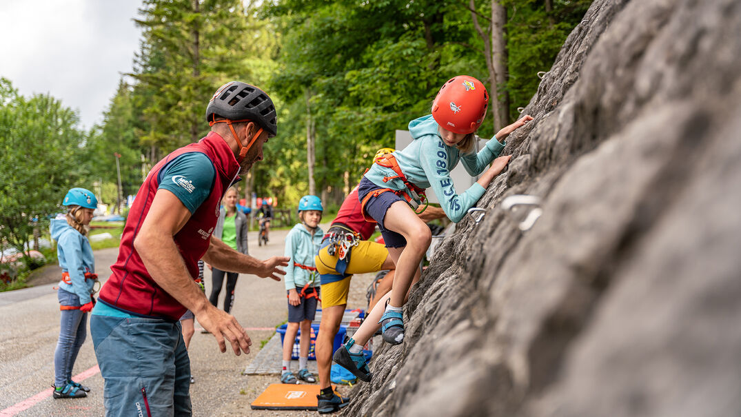 Felskletterabenteuer am Achenseehof in Achenkirch Eine Gruppe Jugendlicher die versuchen die 18 Meter hohe Kletterwand am Achenseehof mit Hilfe eines Guides zu erklimmen.