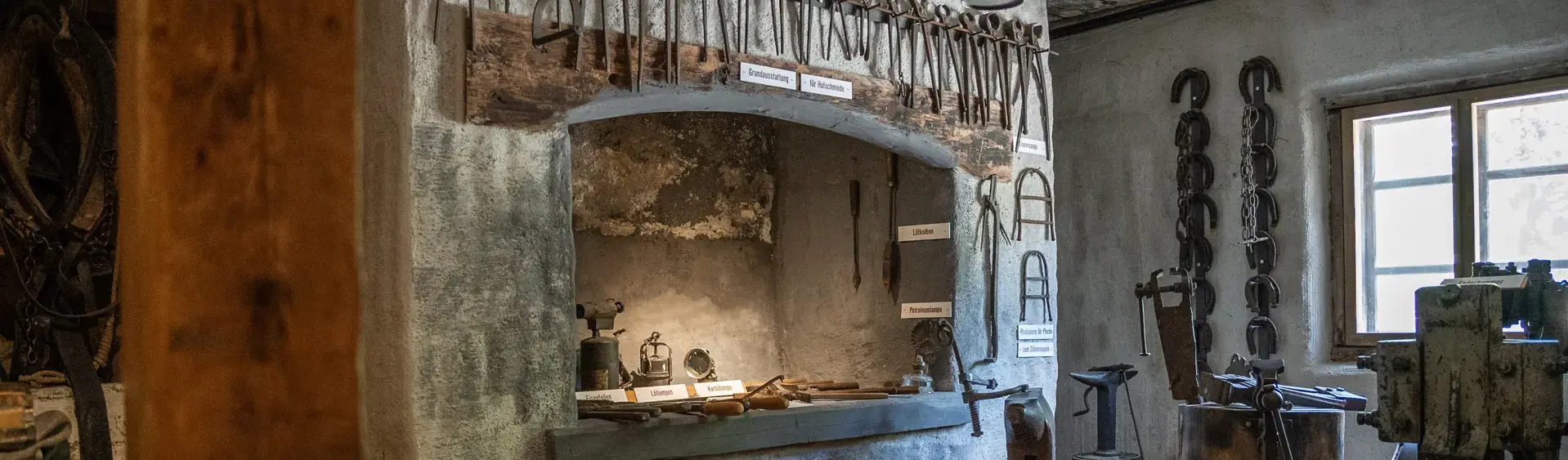 Heimatmuseum Sixenhof in Achenkirch Das Bild zeigt eine historische Schmiede im Heimatmuseum Sixenhof mit verschiedenen Werkzeugen auf einem Regalsystem.