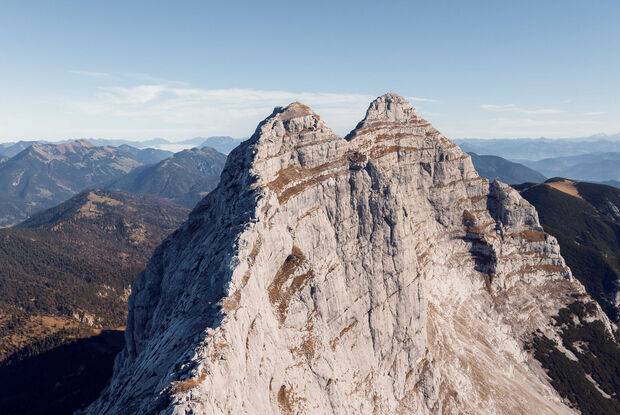 Der Guffert in Steinberg am Rofan Der Guffert in Steinberg am Rofan mit einer markanten, doppelt spitzen Form, umgeben von abwechslungsreicher, bewaldeter Berglandschaft. Die Szenerie zeigt eine klare, blaue Himmel.