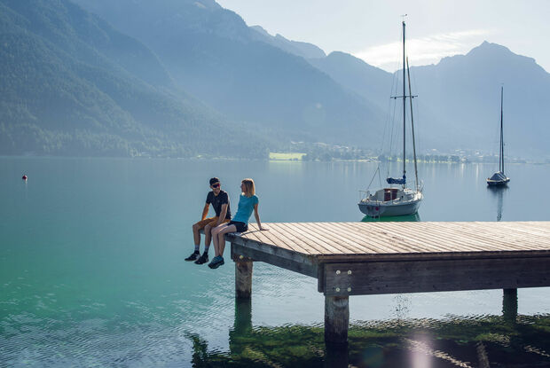 Holzsteg in Pertisau am Achensee Mit dem Partner die Umgebung rund um die Seeuferpromenade und den dazugehörigen Holzsteg in Pertisau erkunden und genießen. Im Hintergrund das Ebner Joch und einige Segelboote.