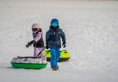 Snowtubing am Achensee Zwei Kinder ziehen ihre Snowtubes hinter sich, nachdem sie die eigens dafür ausgewiesene Piste der Planberg- und Wiesenlifte in Pertisau hinuntergerutscht sind.