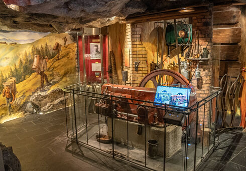 Tiroler Steinöl Vitalberg The image displays a historical exhibit featuring a large vintage machine enclosed in glass, with tools and artifacts arranged around it.