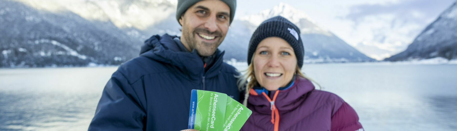 AchenseeCard A couple holds the AchenseeCard up to the camera. In the background, the marvellous winter landscape on Lake Achensee.