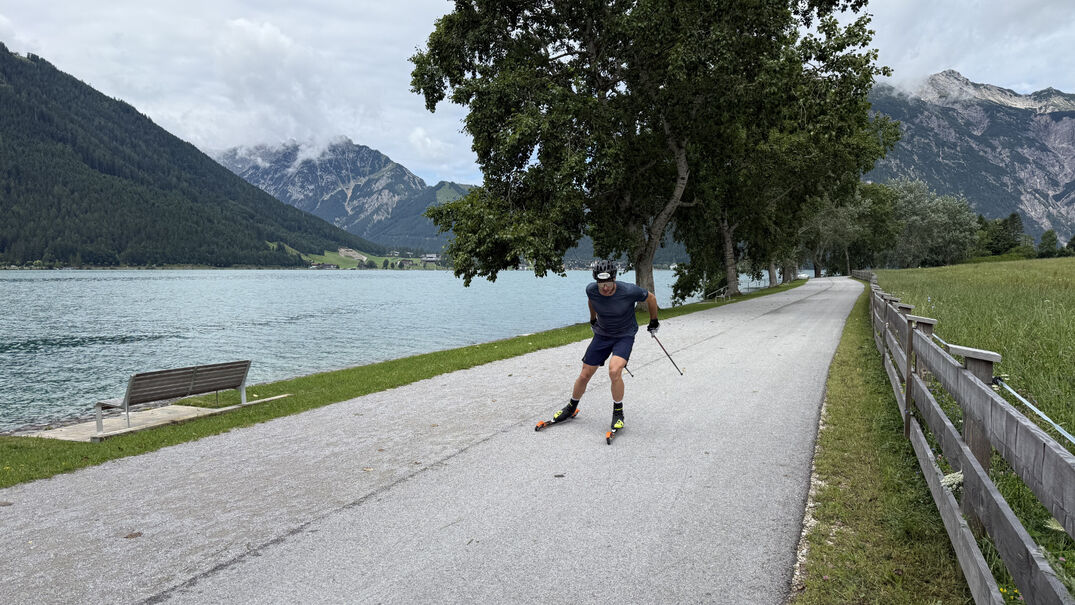 Roller skiing at Lake Achensee A man is skiing on roller skis along a paved path beside Lake Achensee. He is wearing a helmet, gloves and sportswear, and is using poles to propel himself forward.