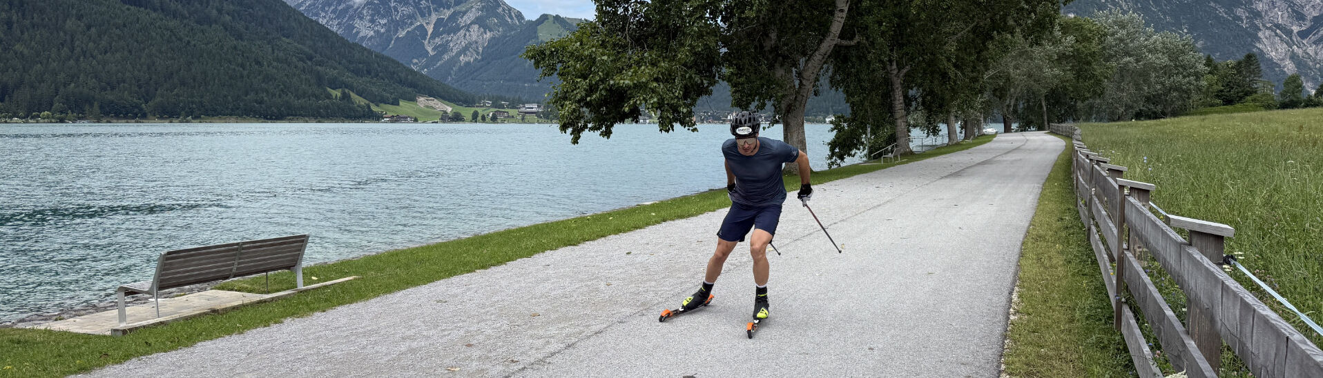 Skirollern am Achensee Ein Mann fährt mit Rollski auf einem asphaltierten Weg entlang eines Achensees. Er trägt einen Helm, Handschuhe und Sportbekleidung und nutzt Stöcke zum Antrieb.
