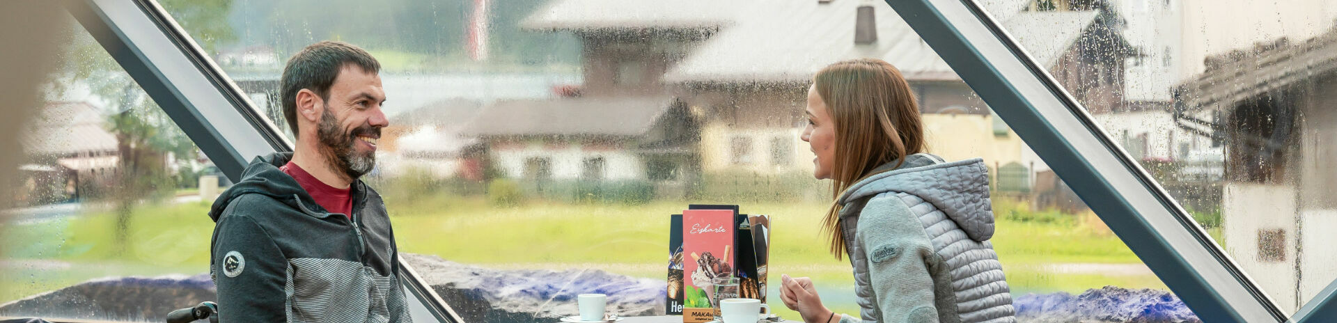 Barrierefreiheit am Achensee Two friends chat over a hot drink at Café Vitalberg. The bar is accessible barrier-free via the panoramic lift.
