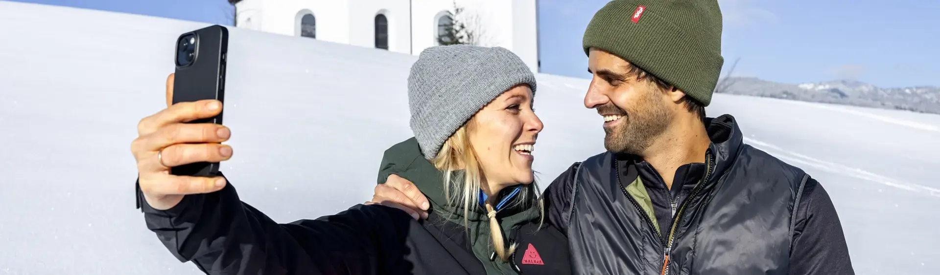 Winterzauber beim Annakircherl in Achenkirch am Achensee Ein Pärchen möchte den schönen Moment, umgeben von einer herrlichen Winterlandschaft und dem Annakircherl im Hintergrund, mit dem Handy festhalten.