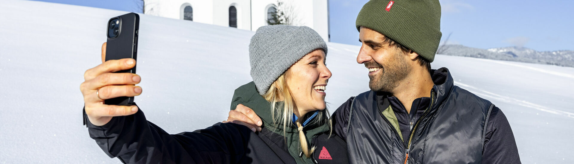 Magical winter at the Annakircherl in Achenkirch am Achensee A couple enjoying the beautiful winter landscape near the Annakircherl chapel, capturing the moment on their mobile phone.