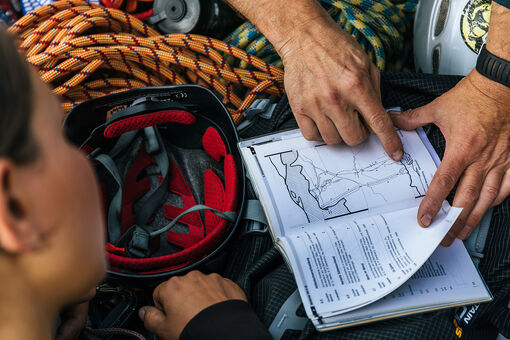 Ein Mann der einer Frau gerade eine Karte erklärt, welche neben einem Kletterhelm und einem Seil liegt.
