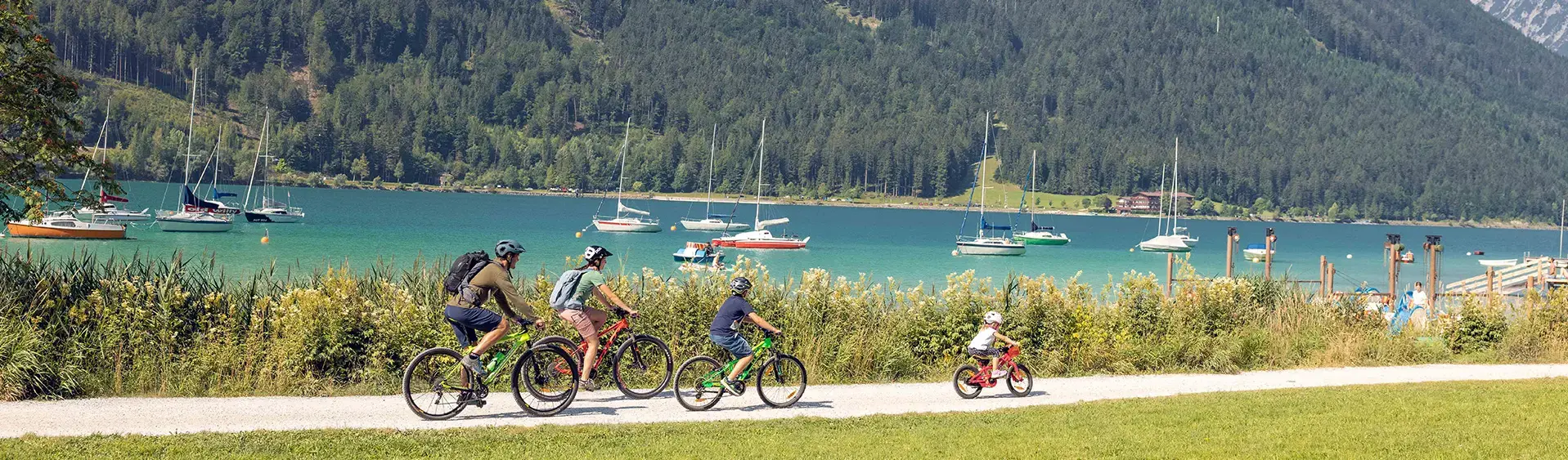 Family bike ride in Maurach am Achensee A family with children explores the lakeshore in Maurach am Achensee by bike. In the background of this photo are several sailboats.