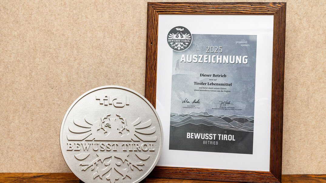 Bewusst Tirol Auszeichnung Ein silbernes Qualitätssiegel mit dem Schriftzug "Bewusst Tirol". Daneben ein gerahmtes Zertifikat mit der Aufschrift "2025 AUSZEICHNUNG" und Informationen über die Unterstützung regionaler Lebensmittel.